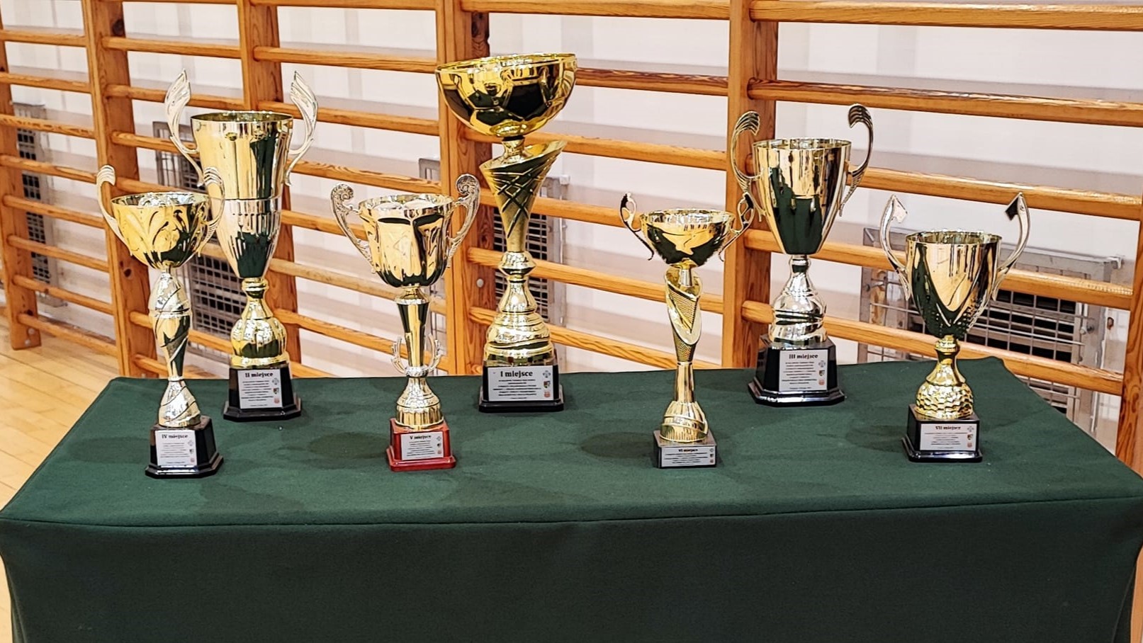Siedem złotych trofeów stoi na stoliku przykrytym zielonym materiałem